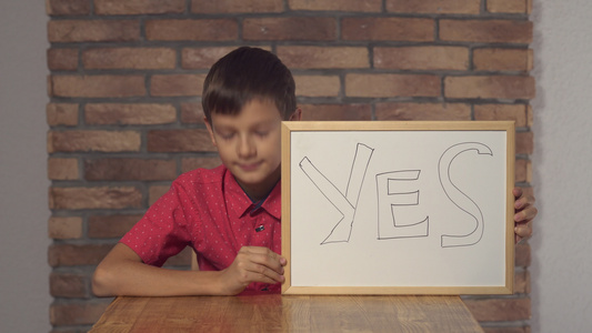 坐在桌子上的孩子拿着翻页图用字母YEA在背景红砖墙视频