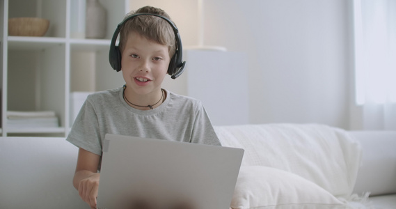 小男孩正在使用带网络摄像头和无线耳机的现代笔记本电脑视频