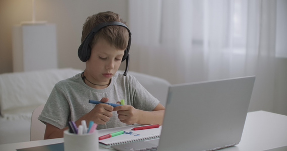 小男孩在家里使用笔记本电脑耳机和彩色铅笔绘画童年快乐视频