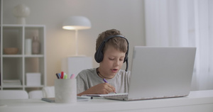 少年男孩正在用耳机绘画和听音乐白天独自坐在家中在画画15秒视频