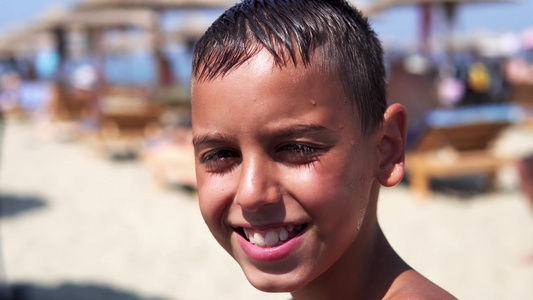 沙滩上帅帅的男孩看着镜头微笑孩子被夏日阳光闪耀着视频