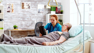 女护理员帮助躺在床上的残疾妇女使用平板17秒视频