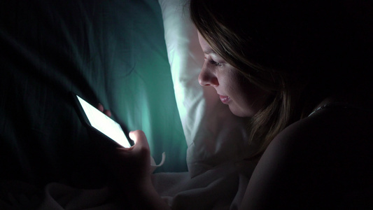 年轻女子在晚上睡觉前在床上使用手机移动成瘾者的概念视频