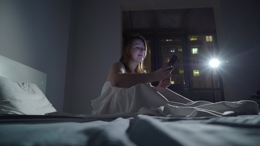 年轻女子在晚上睡觉前在床上使用手机移动成瘾者的概念视频