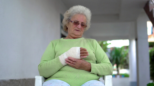 悲伤的老妇女坐在绷带里将伤痕累痛的手放在绷带中视频