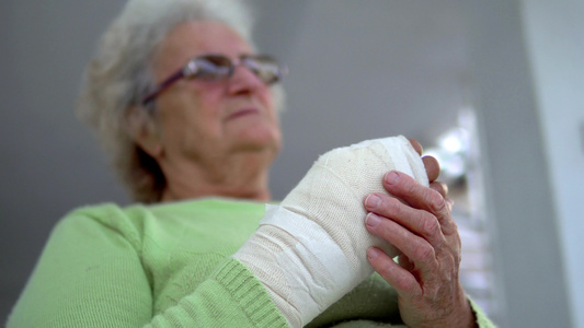 悲伤的老妇女坐在绷带里将伤痕累痛的手放在绷带中视频