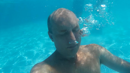 秃头男子潜水水下游泳池和吹泡泡水下观人在度假村的透明视频