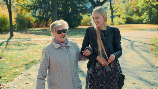 在秋天公园和快乐的金发女孩一起散步的老女人视频