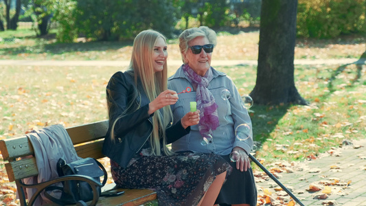 快乐的年轻女子吹泡泡坐在她奶奶一起在公园里坐着视频