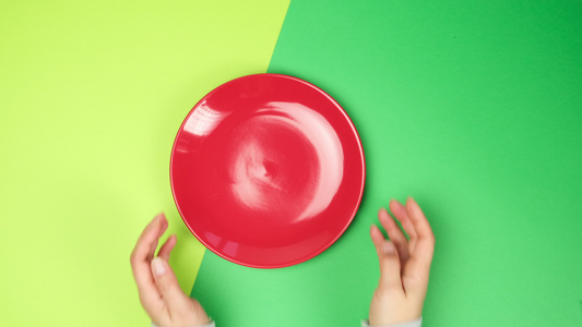 女用手在绿面上放一个空圆圆红陶瓷板顶视图视频