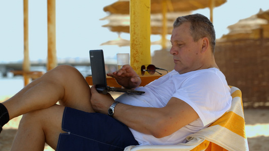 男人在海滩度假胜地用笔记本电脑放松视频
