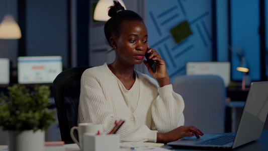 非洲雇员深夜在笔记本电脑上工作时通过电话发言视频