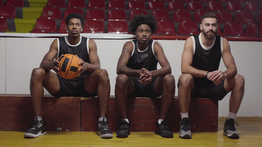3个篮球运动员坐在板凳上观看比赛视频