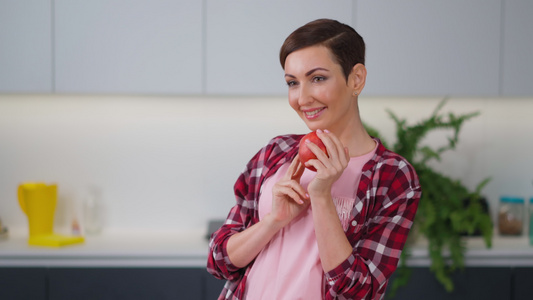 温柔的家庭主妇闻着新鲜的苹果手里拿着它穿着格子衬衫视频