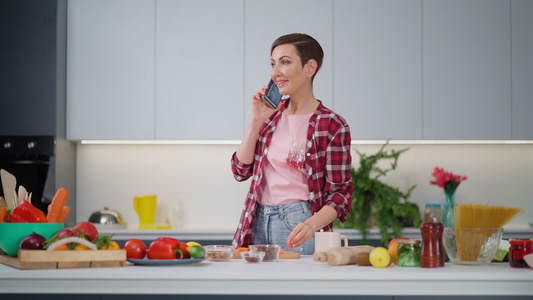 打电话吃胡萝卜留着短发的漂亮女人在厨房准备食物在家视频