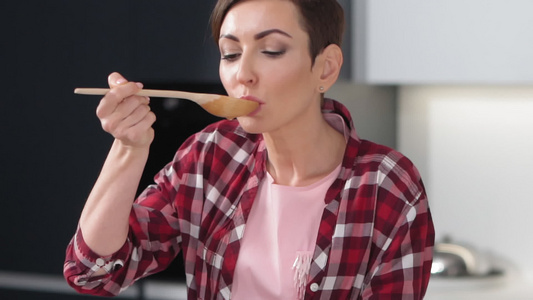 微笑的女人用长木勺品尝站在现代厨房里的熟食在家吃健康视频