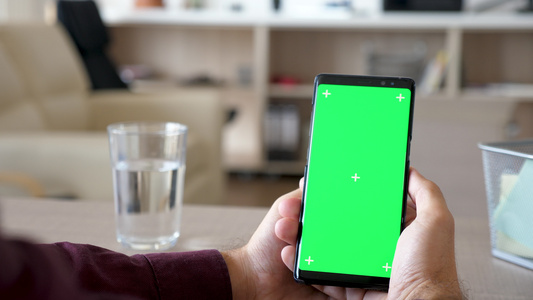 男性手握智能手机的亮光镜头用绿色屏幕染色体模拟视频