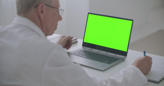 工作医生桌上有绿色屏幕的笔记本电脑男子正在看显示和视频