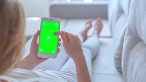 身穿白色牛仔裤的年轻妇女躺在沙发上用绿色屏幕使用智能手机39秒视频