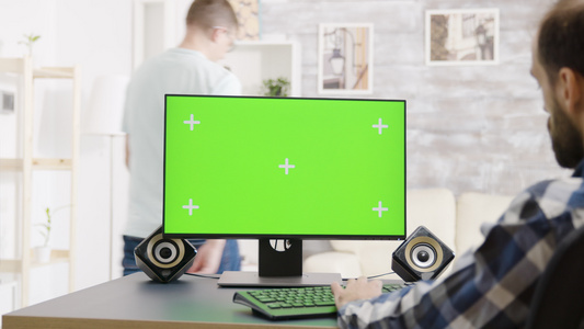 男子在绿色屏幕Pc展示上工作在肩部拍摄视频