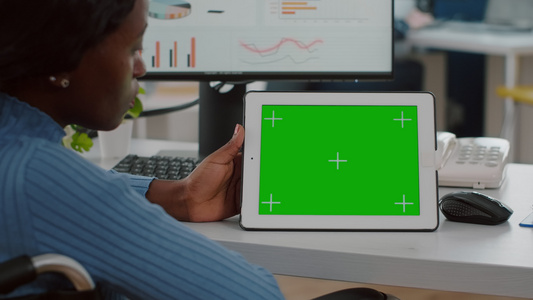 坐在轮椅上看绿色屏幕平板板板的非洲残疾人雇员视频