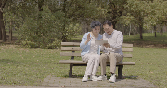 老年夫妇公园长椅上使用平板电脑视频