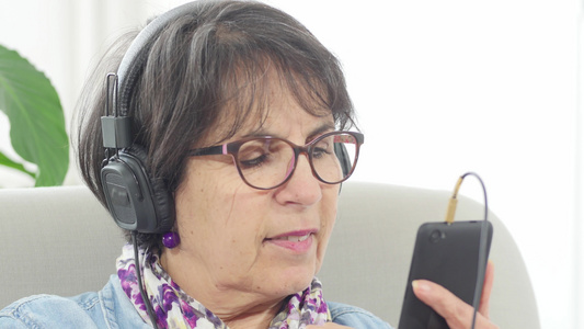 在家用智能手机和耳机听音乐的中中年妇女视频