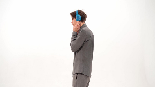 穿着灰色粗呢或套装跳舞的年轻人侧身站着戴着蓝色无线耳机视频