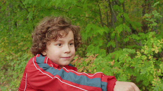 在绿色公园骑自行车的棕色头发的肖像卷发男孩在城市公园视频