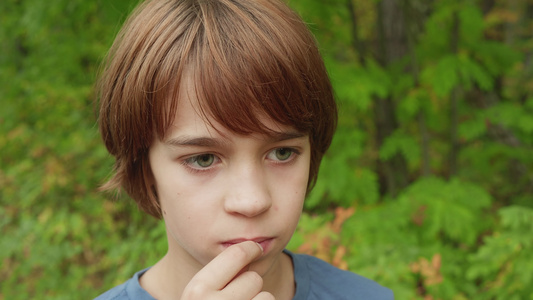 长得英俊的少年男孩在户外嚼口香糖青树背景的年轻男孩视频