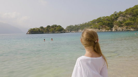 在蓝色的大海和绿色的山景上穿白色连衣裙的肖像少女旅游视频