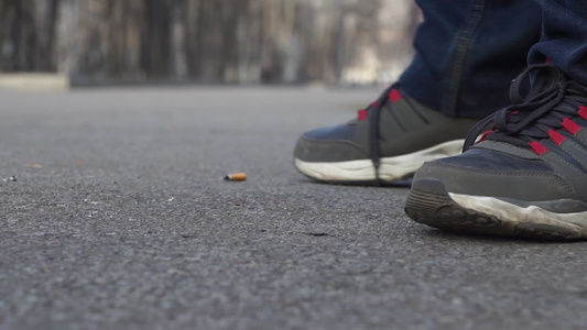 穿着运动鞋和牛仔裤的男子站在一个城市公园中抽烟烟头视频