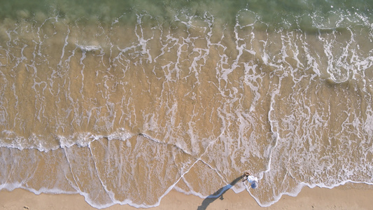 航拍海边沙滩上与海浪玩耍的少女4k素材视频