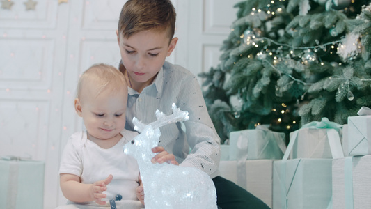 关紧两个可爱的兄弟姐妹坐在圣诞树下拆礼物视频