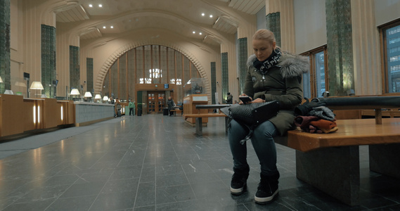 妇女在车站大厅等候并使用智能电话视频
