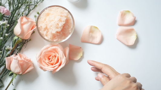 4.k. 自然皮肤护理概念:妇女将白霜用在白色背景的手上,并配有一罐化妆奶油、盐洗涤剂、玫瑰和带复制空间的白花视频