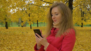 秋天穿着红色斗篷的年轻美女在公园的黄色树林里用手机打字6秒视频