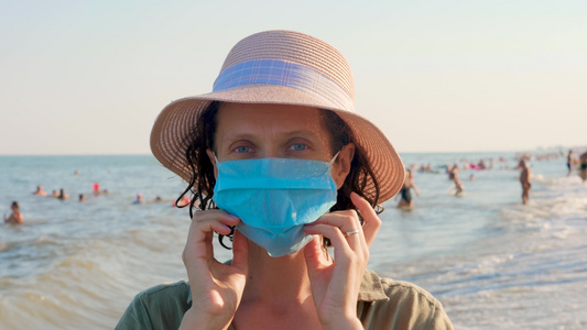 假期和爆发。戴着一次性面具的女人看着相机。海面背景与旅行者在前景中的面罩。预防。戴面具的安全快乐女士视频
