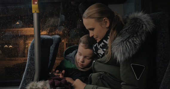 晚上搭乘公共汽车妈妈和孩子在手机上玩视频