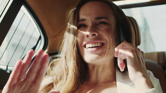 微笑的商业女人欣喜地看到在商车的智能手机上好消息视频