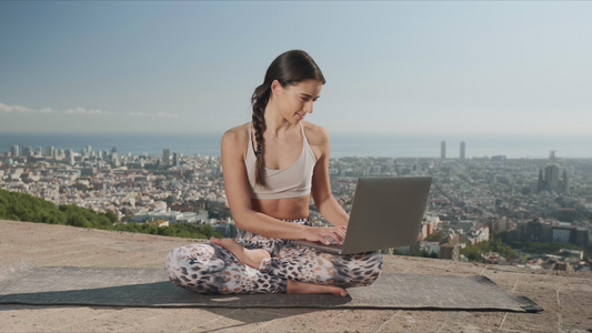瑜伽女孩坐在垫子上用笔记本电脑视频