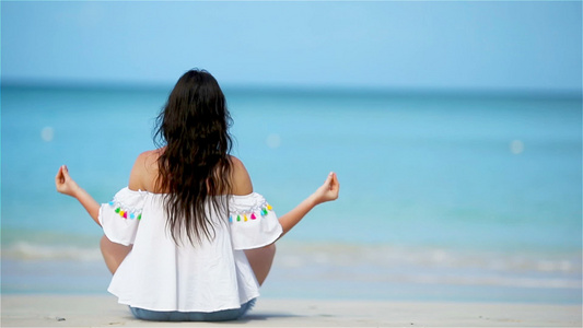 美丽的女孩在热带度假期间的瑜伽位置。健康的年轻女子坐在瑜伽位置，在沙滩上冥想视频