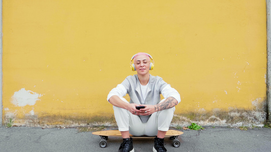 意大利，带着智能手机和耳机的年轻女子坐在滑板上视频