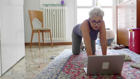 在笔记本电脑前的地板上锻炼的老妇人视频