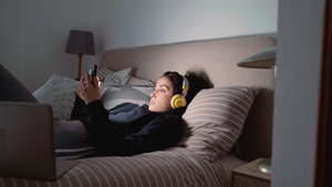 戴着耳机躺在床上使用智能手机的年轻女性13秒视频