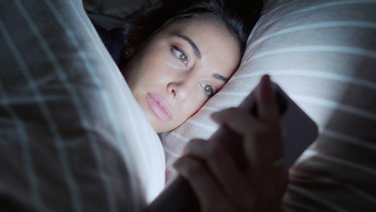 年轻女子躺在床上，看着智能手机视频