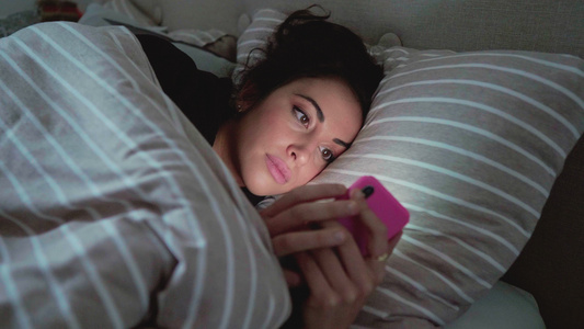 年轻女子躺在床上看着智能手机视频