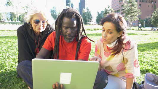 两个留着长发绺的男女坐在公园的草坪上看着笔记本电脑视频