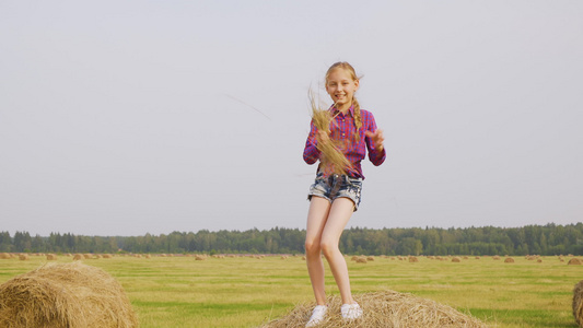 顽皮的女孩在收割田手里拿着稻草在干草堆上跳舞视频