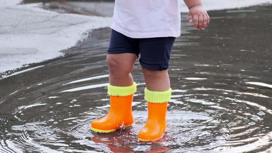 小孩穿着橙色靴子在雨后在水坑里玩视频